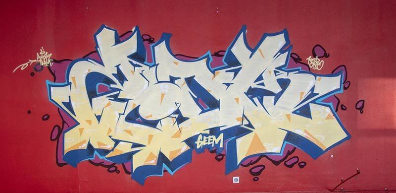 graffiti de Kzed axdk fond rouge et lettrage degradé de jaune avec un contour bleu foncé